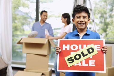 Boy holding For Sale sign with SOLD on it, man and woman packing in the background clipart
