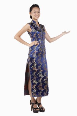 Cheongsam 'lı bir kadın, hoş bir el hareketiyle gülümsüyor.
