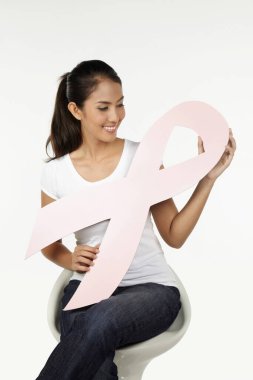 Sandalyede oturan mutlu kadın pembe göğüs kanseri kurdelesini tutuyor.