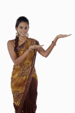 Sari giymiş bir kadın el hareketleriyle gülümsüyor.