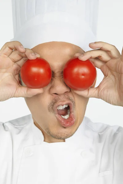 Azjatycki Kucharz Trzymający Pomidory Przed Oczami Śmiesznym Wyrazem Twarzy — Zdjęcie stockowe