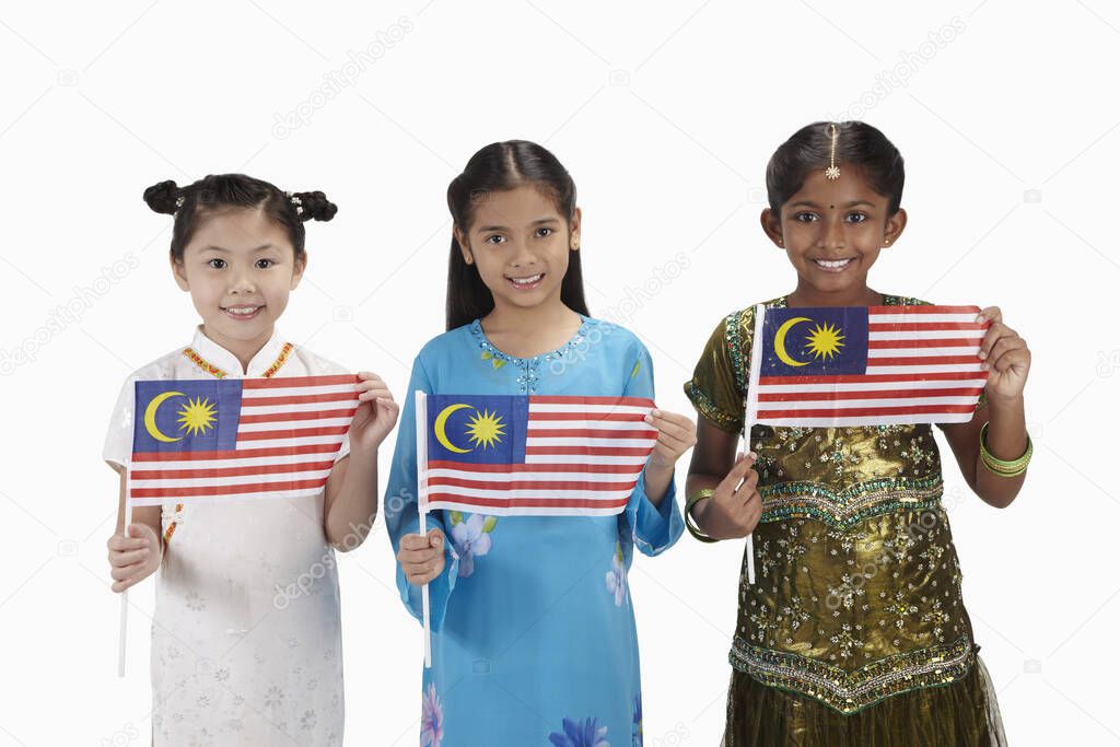 Girls in traditional clothing smiling and each holding a Malaysian flag