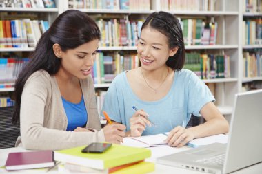 İki öğrenci kütüphanede birlikte okuyorlar.