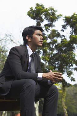 Genç Asyalı işadamı bir bankta oturuyor.