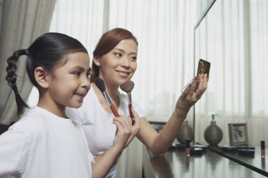 Anne ve kızı yüzüne makyaj yapıyor.