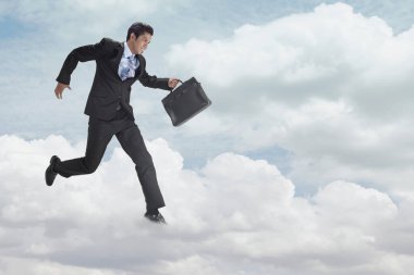 Genç işadamı bulutların üzerinde koşuyor.