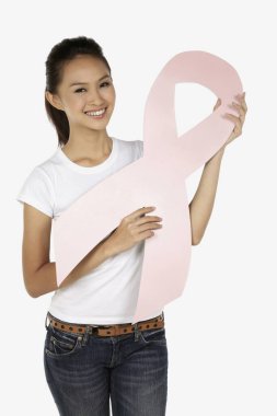 Elinde pembe meme kanseri kurdelesiyle gülümseyen bir kadın.