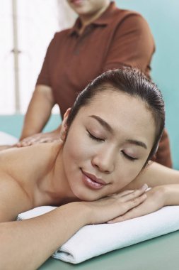 Önünde yatan genç bir kadın sırt masajı yaptırıyor.