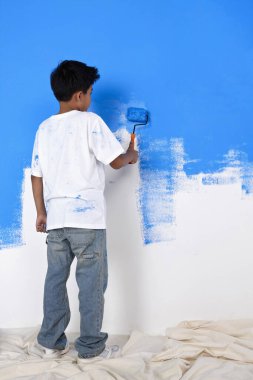 Boya silindirli duvarı boyayan çocuk.