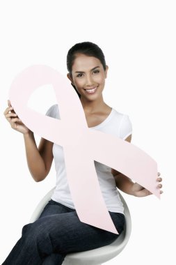 Sandalyede oturan mutlu kadın pembe göğüs kanseri kurdelesini tutuyor.