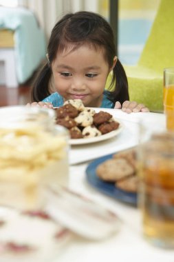 Bir tabak kurabiyeye bakarken gülümseyen kız.