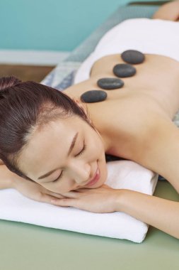 Önünde uzanmış sırtına masaj taşı takmış, rahatlayan genç bir kadın.
