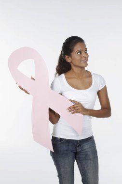 Elinde pembe meme kanseri kurdelesiyle gülümseyen bir kadın.