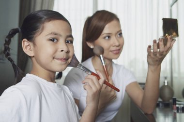 Anne ve kızı yüzüne makyaj yapıyor.