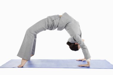 Yetişkin bir iş kadını yoga pozisyonunda geriye doğru eğiliyor.