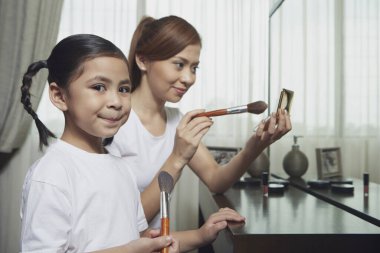 Anne ve kızı yüzüne makyaj yapıyor.