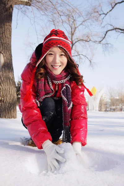 Kalın elbiseli kadın kartopu yapıyor.