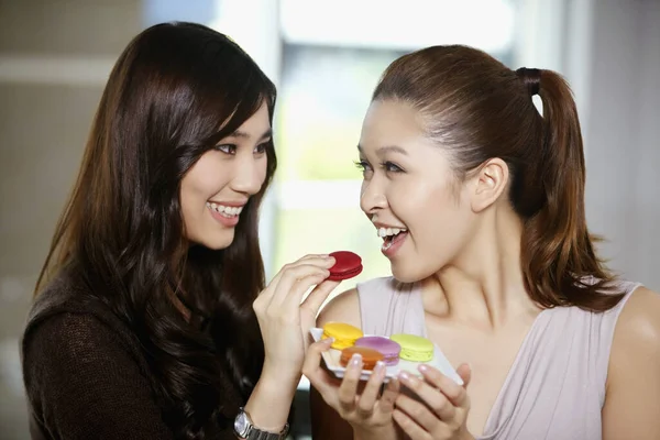 Bir kadın başka bir kadına kurabiye yediriyor.