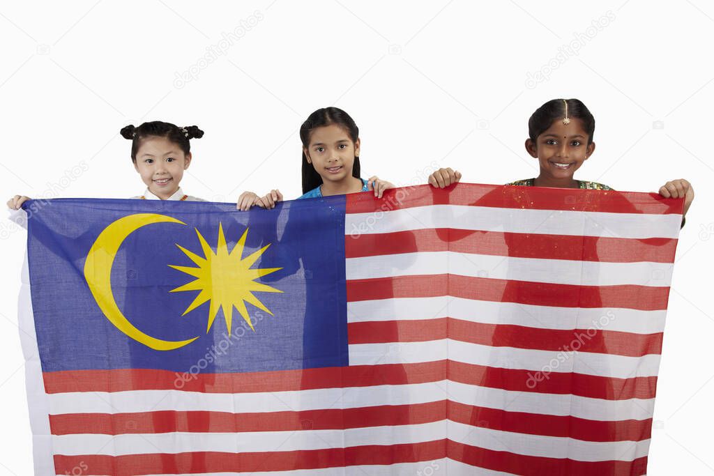 Girls in traditional clothing smiling holding a big Malaysian flag