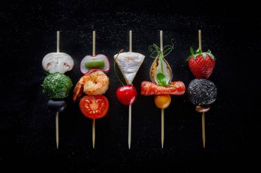 Peynirli kanepe, çilek, karides, mantar, vişneli domates ve siyah bir masanın üzerinde zeytin. Yemek servisi. Ziyafet..