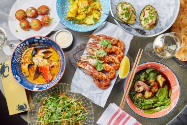 Taş bir masanın üzerinde deniz ürünleri tabakları olan yemek masası, deniz ürünleri tabakları: Tom Yam çorbası, ızgara karides, ızgara avokado, bir bardak beyaz şarap ve bir lahana salatası, kopyalama alanı.  