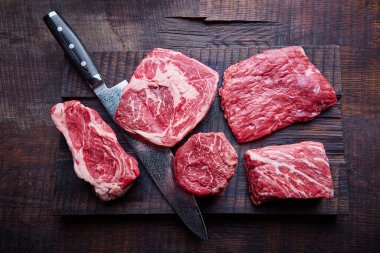 Tahta bir tahtanın üzerinde çiğ biftek çeşitleri, bir bıçak, taze çiğ et, fotokopi alanı, üst görünüm