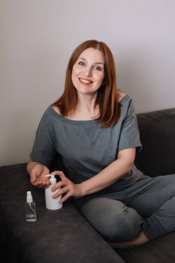 Yetişkin kadın portresi ellerini temizliyor ve evdeki oturma odasında bir kanepede oturuyor. Coronavirus konsepti