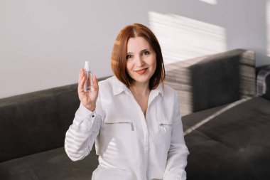 Kadının elinde dezenfektan spreyi var ve kameraya bakıyor. Yetişkin bir kadın antibakteriyel el temizleyici kullanır..