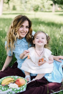 Genç bir anne küçük kızıyla oynar ve parktaki kameraya bakar..