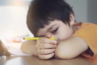 Ödevi için tablet kullanan kendini izole etmiş bir okul çocuğu derin düşüncelere dalmış üzgün bir çocuk.
