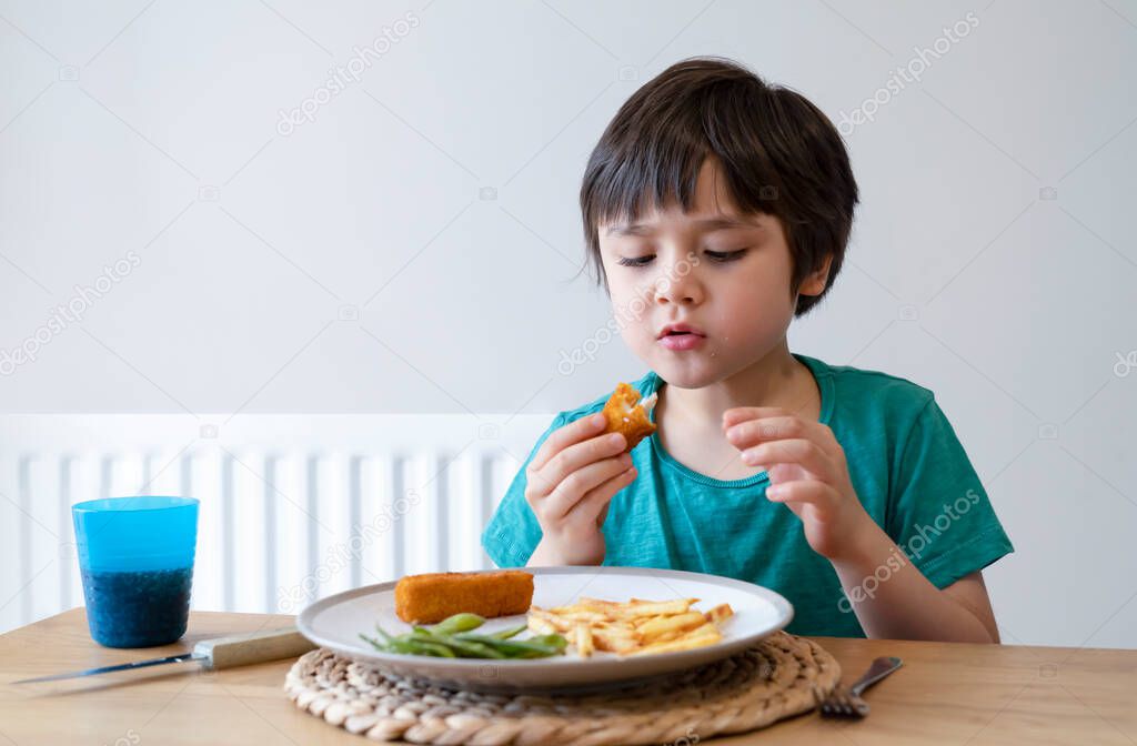 Portrait of 5 year old kid boy having homemade fish finger and french fries for Sunday dinner at home, A happy child eating lunch, Children eating heathy and Fresh food, Healthy life style concept