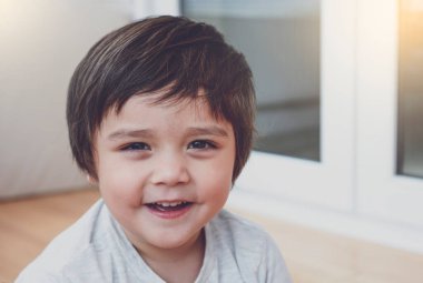 Gülümseyen yüzüyle kameraya bakan mutlu küçük çocuğun portresi, çocuk odasında oynayan sağlıklı çocuk, bahar ya da yaz aylarında hafta sonları evde dinlenen pozitif çocuk.