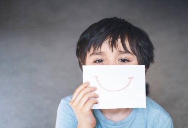 Üzgün yüzlü, elinde gülümseyen beyaz kağıtlarla sıkılmış çocuk portresi, kendini tecrit ve karantina süresince evde kalan çocuk. Coronavirüs salgını ve grip salgını 