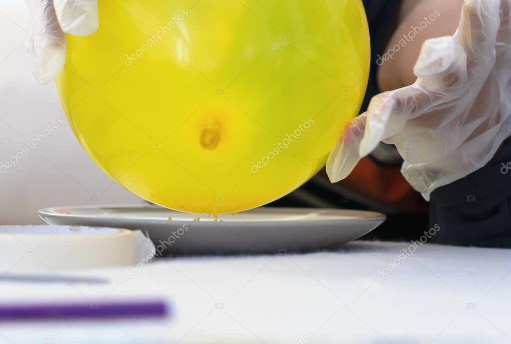 Cropped shot kid hand holding balloon above plate of dry gelatin crystals, School kid doing science project, experiment with gelatine and static charged balloon, science experiment concept