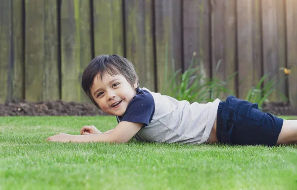 庭の緑の芝生の上に横になって楽しんでいるアクティブな子供 芝生の上に寝そべっている健康な子供の男の子夏の日のコンセプトを楽しむ幸せな子供時代 — ストック写真