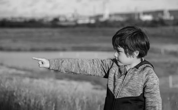 Portrait black and white photo of happy little boy pointing finger up , Active kid having fun playing in farm field with bright light sunny day. , Child playing outdoor with blurry natural background.