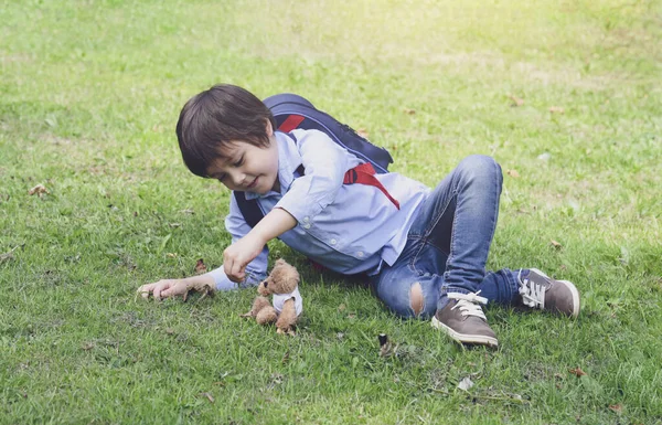 可爱的小男孩背着背包躺在草地上 在公园里和玩具熊玩耍 快乐的孩子脸上挂着笑脸 春天或夏天在户外玩玩具 — 图库照片