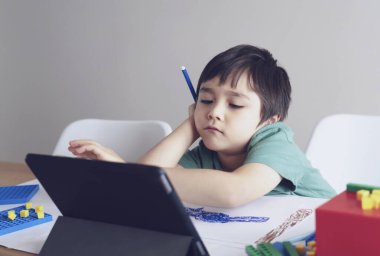 Ödevi için tablet kullanan kendini izole etmiş bir okul çocuğu derin düşüncelere dalmış üzgün bir çocuk.