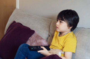 Portre çocuğu elinde uzaktan kumandayla kanepede oturuyor, içten içe evde oturup televizyon seyreden mutlu bir çocuğa kısa devre yaptırıyor, yaz tatilinde çocuklar için etkinlik düzenliyor..
