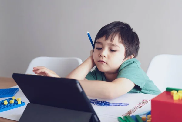 School kid in self isolation using tablet for homework,Child sad face lying head down looking out deep in thought, Boy stay at home during covid-19 lock down