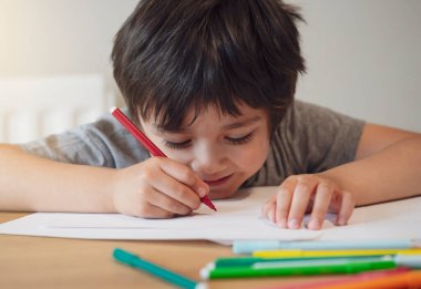 Öğrenci çocuğun masa başında oturup ödev yapması, Mutlu Çocuk 'un elinde kırmızı kalem tutması ya da beyaz kağıda çizmesi, ilkokul ve evde eğitim konsepti.