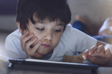 Ödev için tablet kullanan okul çocuğu, kanepeye uzanıp derin düşüncelere bakan üzgün suratlı çocuk, covid-19 kilitlenirken evde kalmaktan sıkılmış çocuk, çevrimiçi eğitim alan sosyal mesafe.