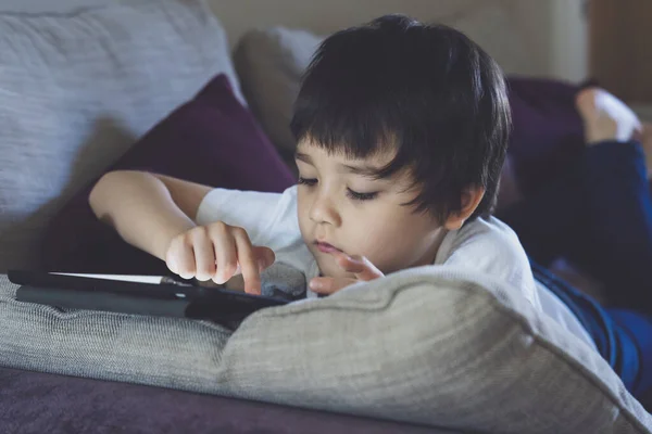 School kid using tablet for homework, Child lying down on sofa tuching on sceeen, Bored Boy stay at home during covid lock down,Social Distancing, learning online , Distnace Educationeducation concept