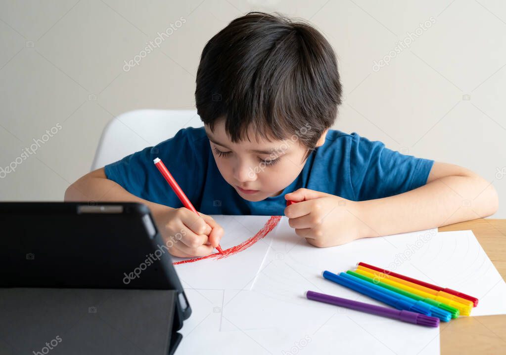 Kid coloring his own rainbow drawing on paper,Child using digital tablet searching information on internet for his home work,Home schooling Social media campaign for coronavirus prevention concept