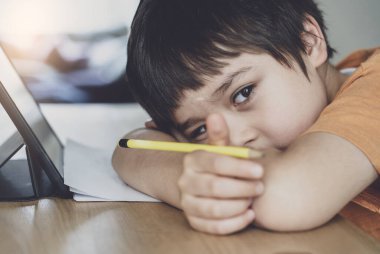 Ödevi için tablet kullanan kendini izole etmiş bir okul çocuğu derin düşüncelere dalmış üzgün bir çocuk.