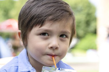 Yüzü gülen tatlı çocuk yazın bulanık soğuk bir içecek içerken, Candid parkta oturup soda ya da pipetle alkolsüz bir içecek içen Mutlu Çocuk 'u vurdu.