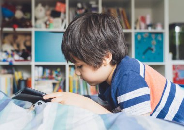 Ödevi için tablet kullanan çocuk izolasyonu, dijital tablet kullanarak yatakta yatmak internet, evde eğitim, sosyal mesafe, e-öğrenim çevrimiçi eğitim