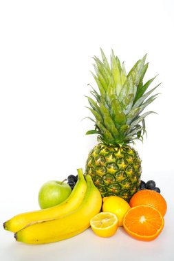 Beyaz arka planda, tam bir ananas, yeşil elma, muz, portakal, dilimlenmiş limon ve bir demet siyah üzüm içeren tropikal meyve seçimi.