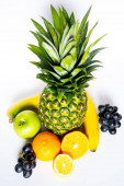 A trópusi gyümölcsök választéka egyszerű fehér háttér mellett, beleértve egy egész ananászt, zöld almát, banánt, narancsot, szeletelt citromot és egy csomó fekete szőlőt