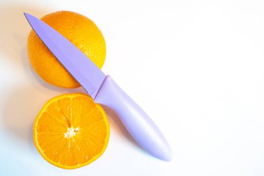 İki yarım portakal ve düz beyaz bir arka planda keskin bir bıçak.